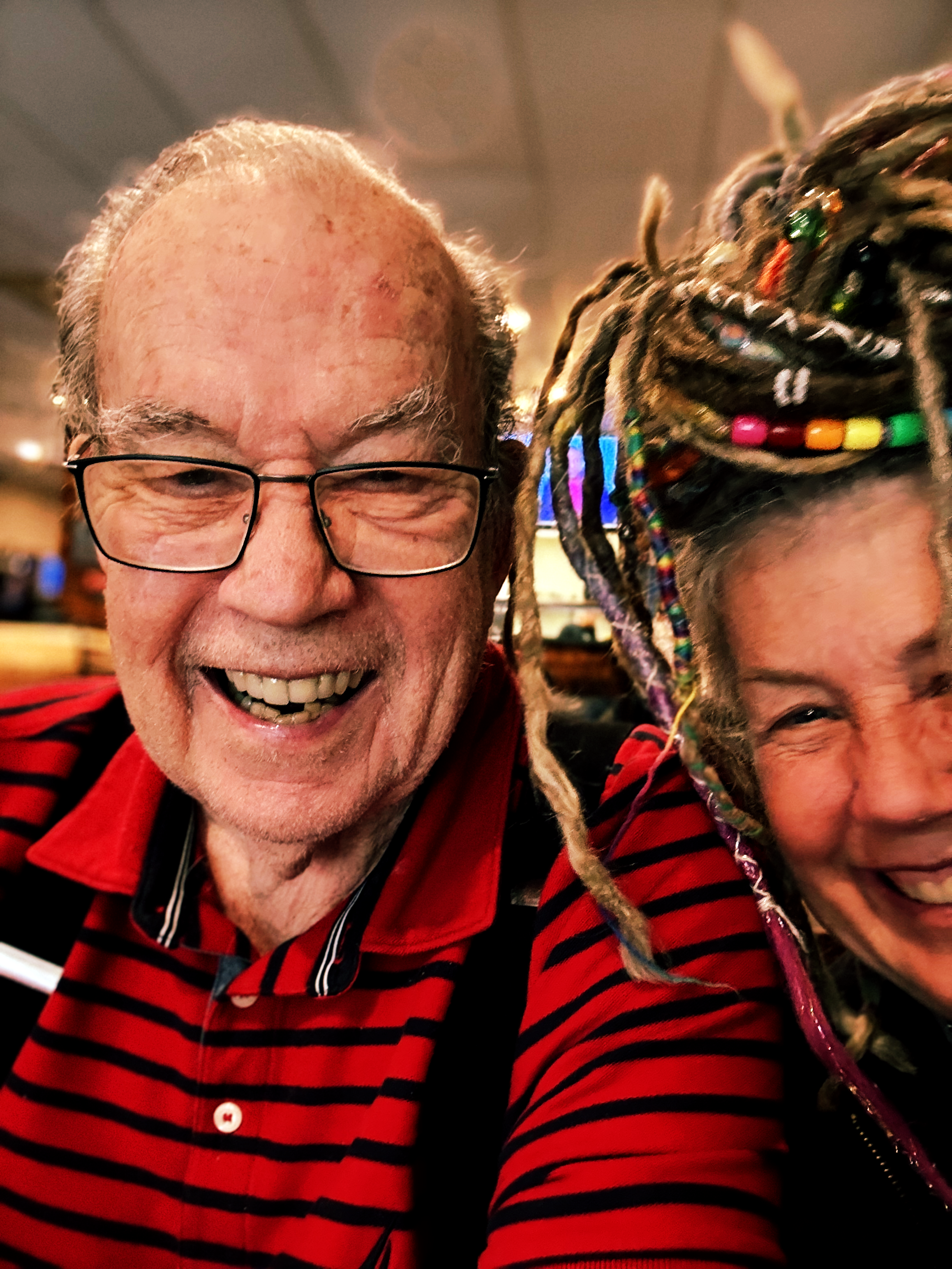 Close-up selfie of an older man in glasses smiling beside a woman smiling, both leaning into the frame.