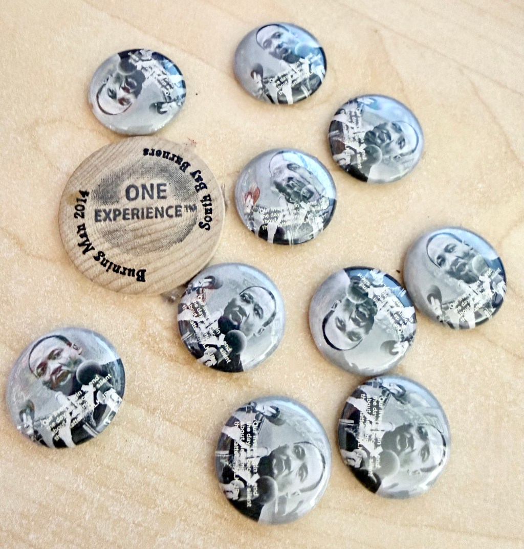 Black-and-white Martin Luther King Jr. quote buttons on a wooden surface, next to a “ONE EXPERIENCE” button.